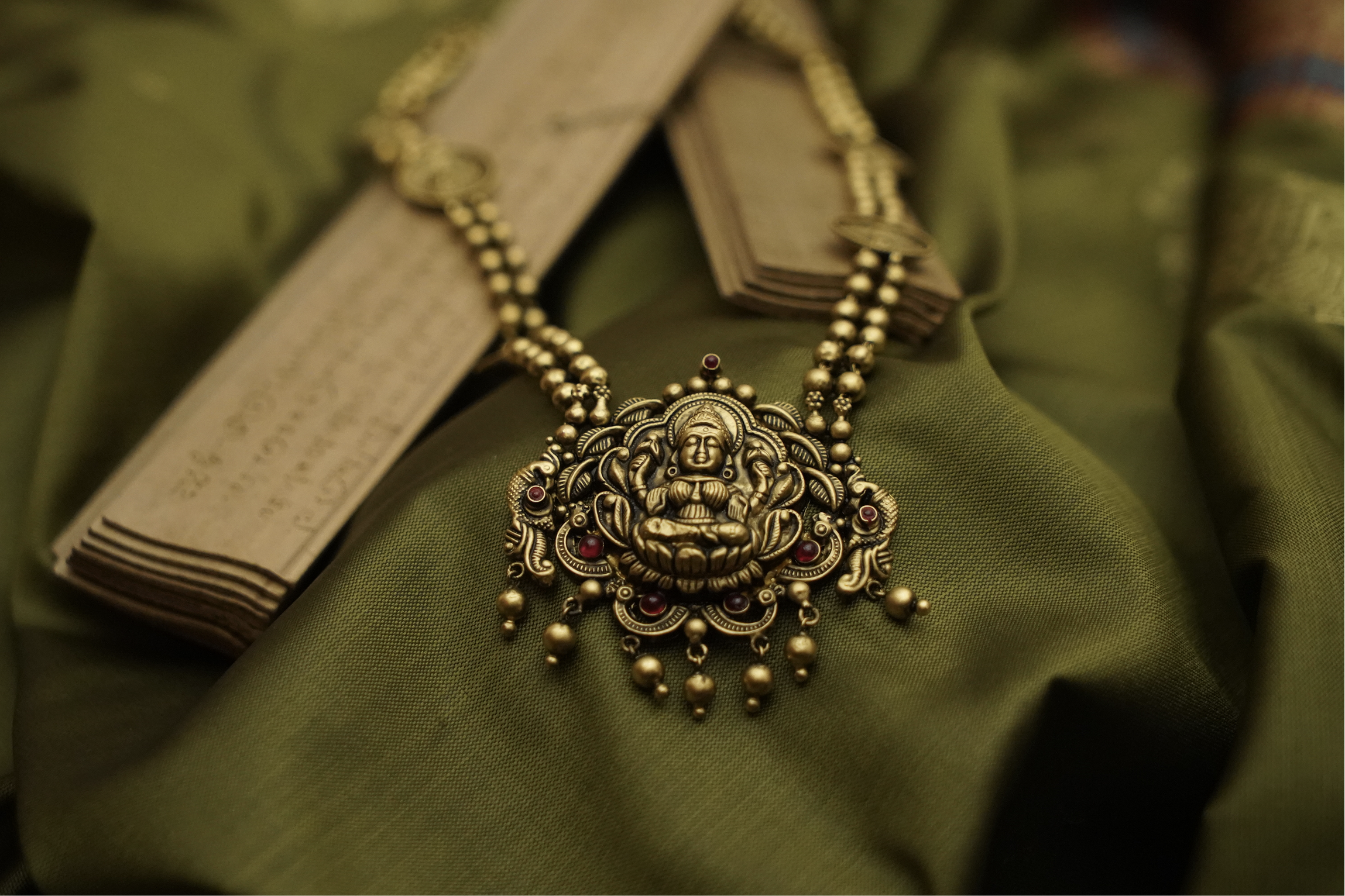 Lakshmi pendant necklace draped over ancient Kerala palm leaf manuscripts