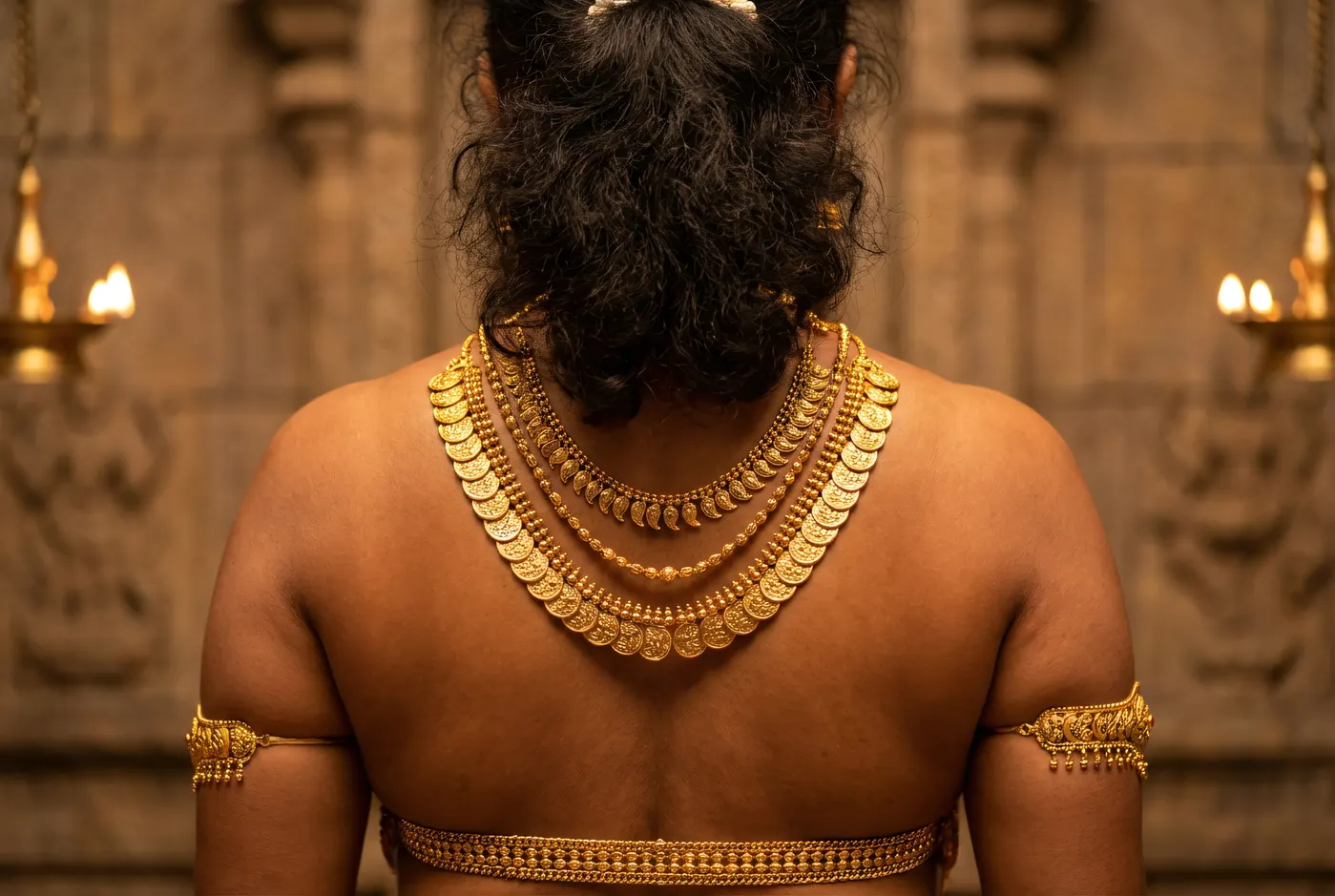 Back view of model wearing layered gold necklaces in temple, dramatic lighting